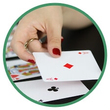 En dealer delar ut kort vid ett spelbord. I handen håller dealern ruter ess och på bordet skymtas klöver ess.